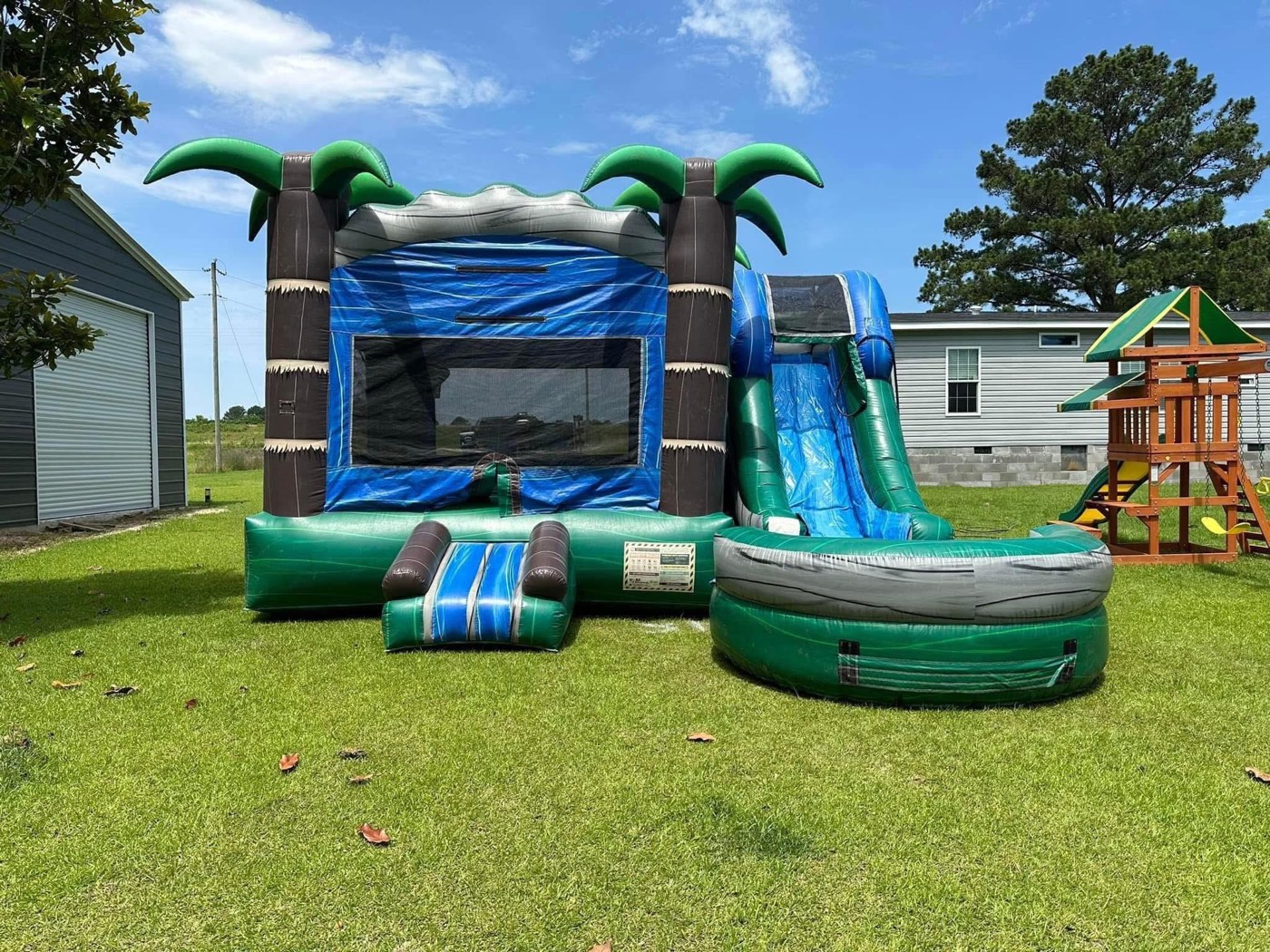 Emerald green tropical palm themed bounce house with slide and splash pool